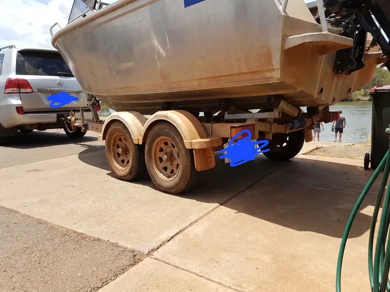 Customer photo of an alloy boat on a tandem trailer at a river ramp, hull sides and mudguards filmed with red dust, tow vehicle hitched in front. The number plates have been scribbled out.